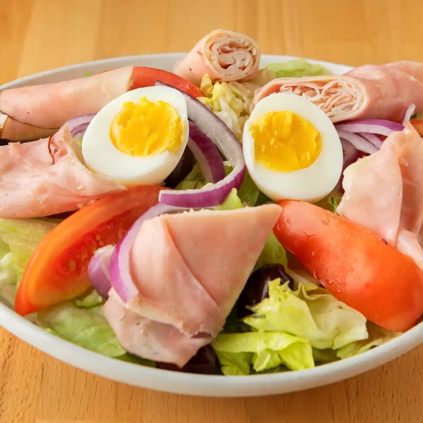 A fresh salad with lettuce, tomatoes, red onions, hard-boiled eggs, and rolled deli meats.