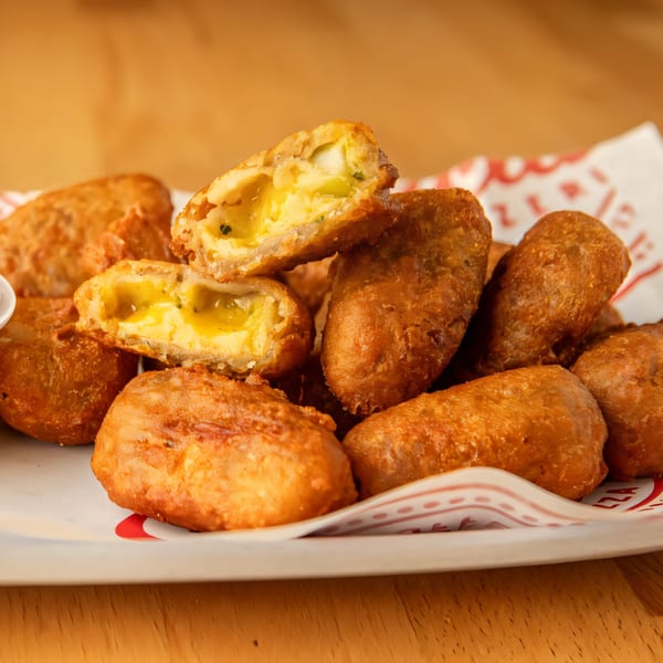A close-up of golden-brown fried jalapeño poppers, some cut open revealing melted cheese and peppers.